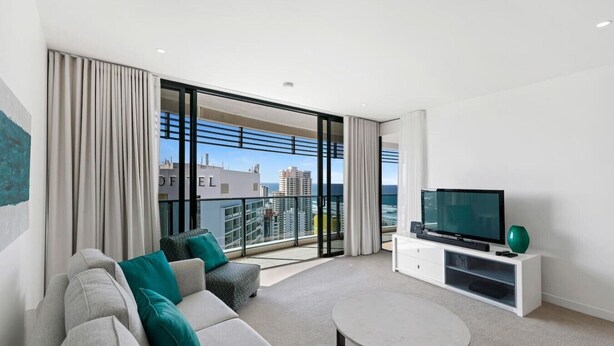 Un soggiorno moderno con divano, tavolino, televisore e un balcone con vista sulla città.