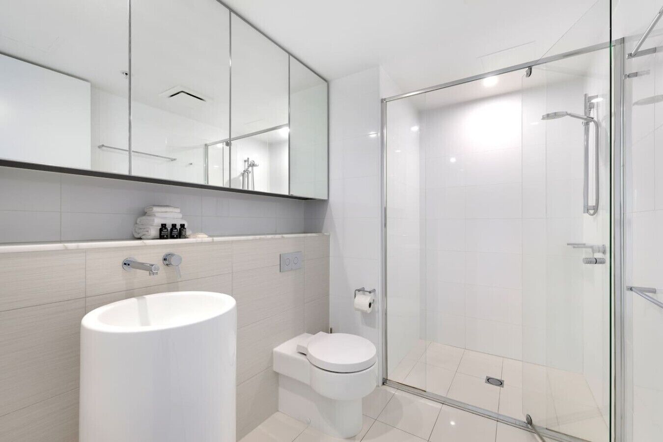 Ein modernes Badezimmer mit einem großen weißen Waschbecken, einer Toilette, einer Duschkabine aus Glas und einem Spiegel über dem Waschbecken.
