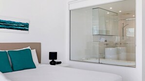 Una camera d'hotel con un letto grande, un comodino con una lampada, un box doccia in vetro e un quadro appeso al muro.
