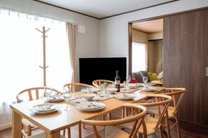 A dining area with a wooden table set for four, chairs, a coat rack, and a television. - Nakafurano Nature Retreat (Sorachi-gun,Nakafurano-cho)