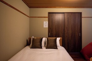 A bedroom with a bed, two pillows, a wooden wardrobe, and a red chair.