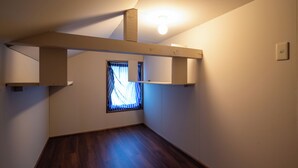 Ein Zimmer mit schrägen Wänden, einem fensterartigen Ausblick mit Vorhängen, einer Leuchte und einem Thermostat.