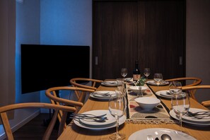 A dining table set for six with chairs, a television, and a bottle of wine.