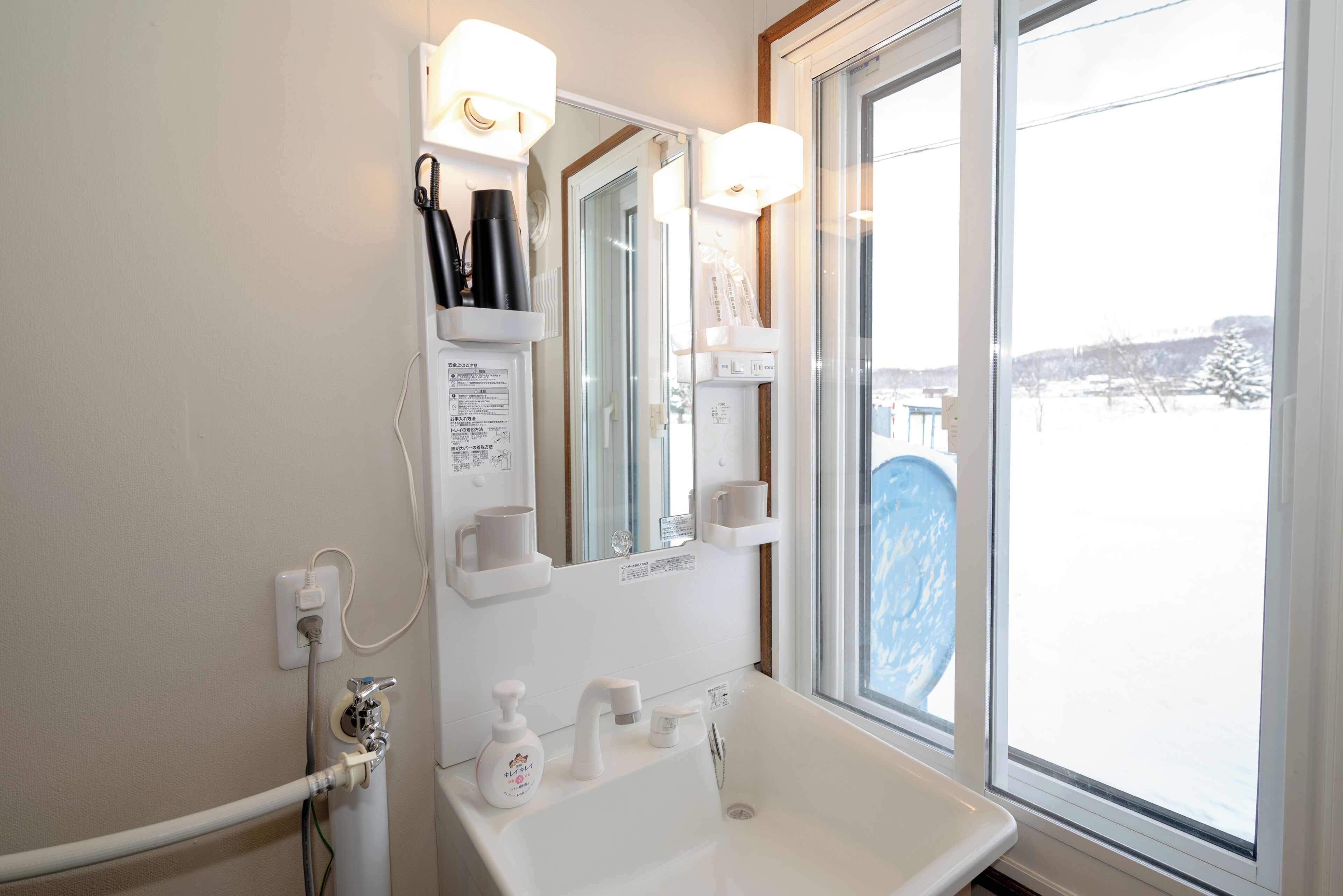 Un baño con lavamanos blanco, espejo y estantes con artículos de tocador.