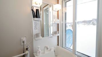 Un baño con lavamanos blanco, espejo y estantes con artículos de tocador.