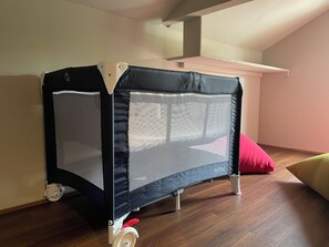 A foldable playpen with wheels, a red cushion, and a wooden floor.