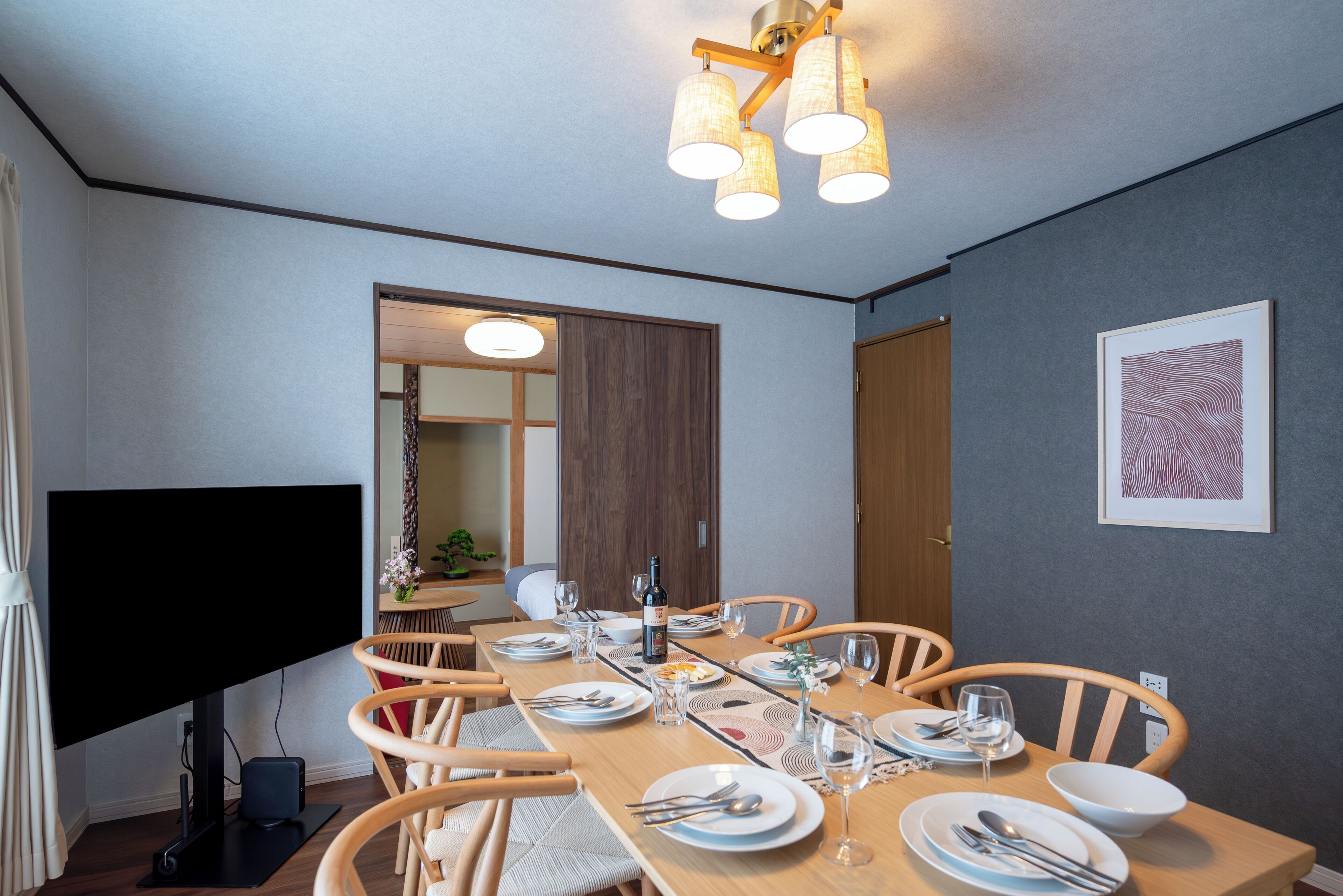 En matplats med ett långt bord som är dukat för fyra personer, en platt-TV och en taklampa.