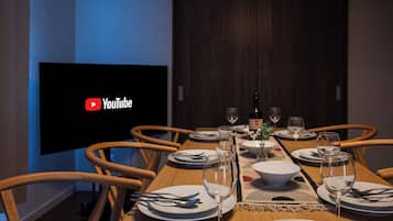 A dining room with a wooden table set for six, a flat-screen TV, and a dark wooden door.