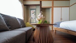 Ein Zimmer mit einer Couch, einem Bett, einem Holztisch mit einer Vase und einer traditionellen japanischen Schiebetür.