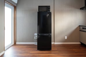 A black refrigerator with a microwave on top, a power outlet, and a window on the left. - Nakafurano Nature Retreat (Sorachi-gun,Nakafurano-cho)