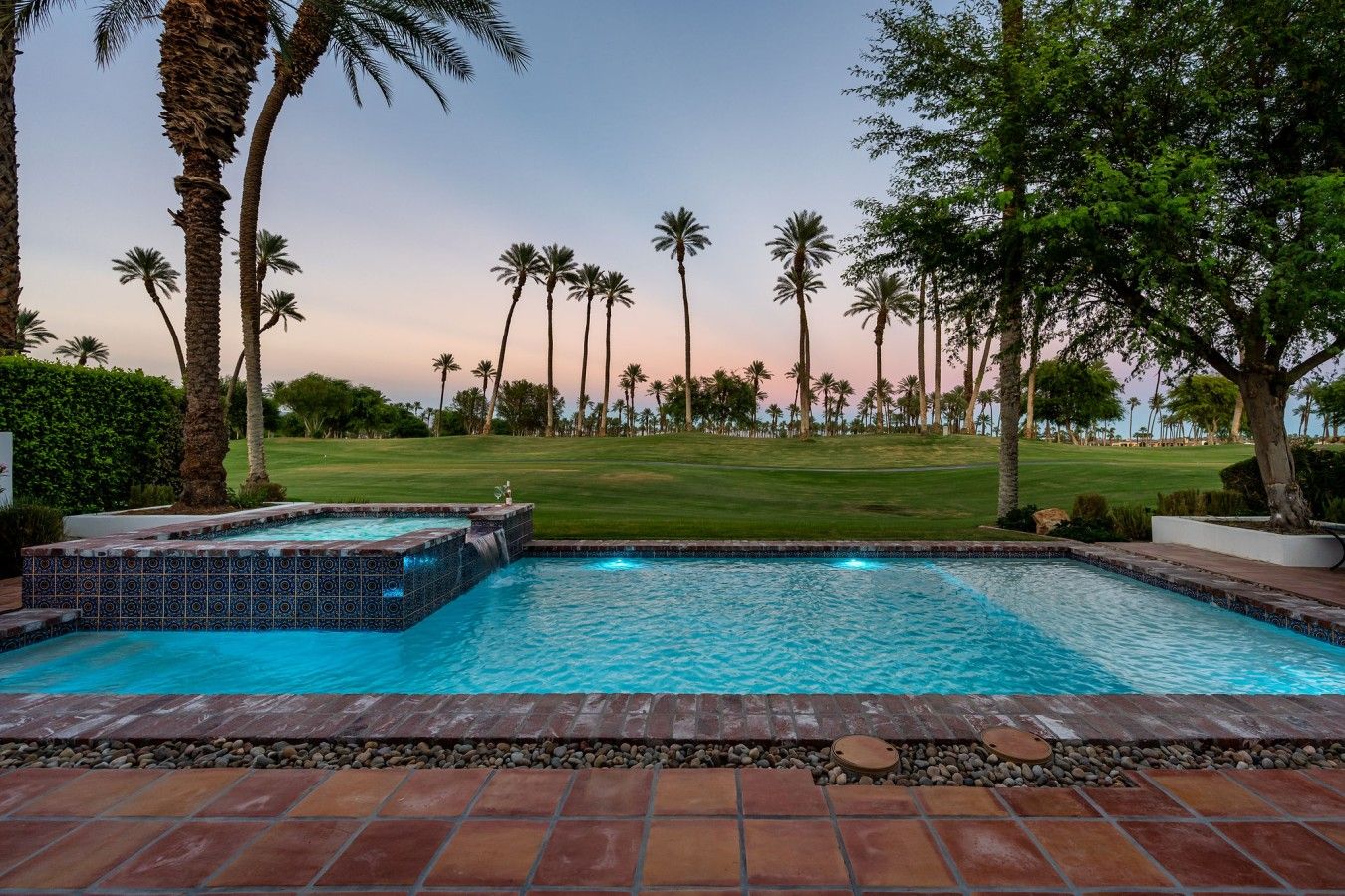 Een zwembad met een jacuzzi, omringd door palmbomen en een golfbaan op de achtergrond.