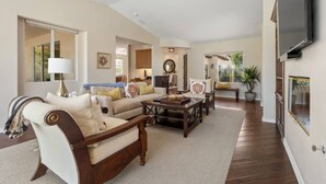 A spacious living room with a sofa, coffee table, and a television mounted on the wall. - Little Sol at The Palms Golf Club (La Quinta)