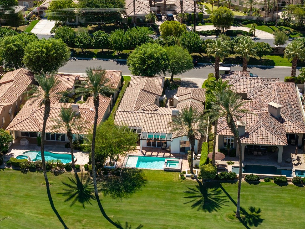 A residential area with multiple houses, each featuring a swimming pool and surrounded by palm trees.