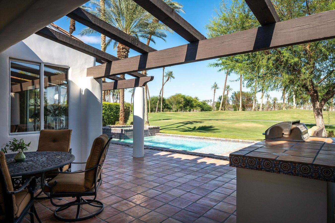 An outdoor patio with a pool, seating, and a view of a golf course.