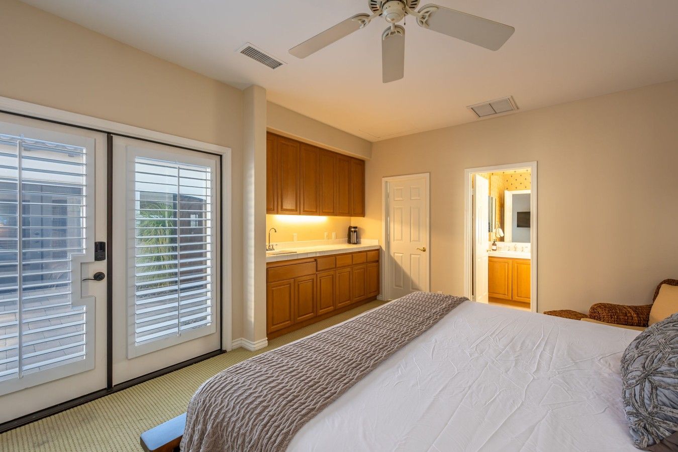 A bedroom with a bed, a ceiling fan, a sliding glass door, and a kitchen area visible through an open door.