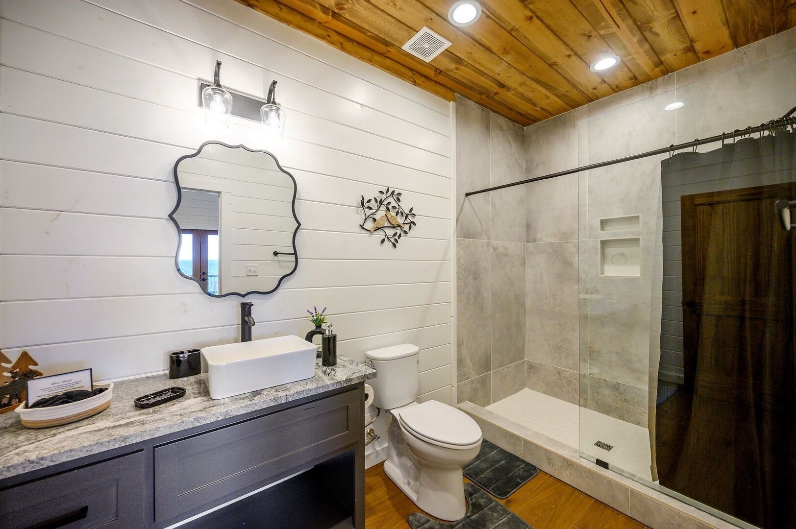 Une salle de bain avec un lavabo blanc, des toilettes, une douche avec des portes en verre et un plafond en bois.
