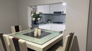 A modern dining area with a glass-top table, white chairs, and a kitchen in the background. - Fabulous 3-bedroom house in enjoyable Ensenada for your getaway (Ensenada)