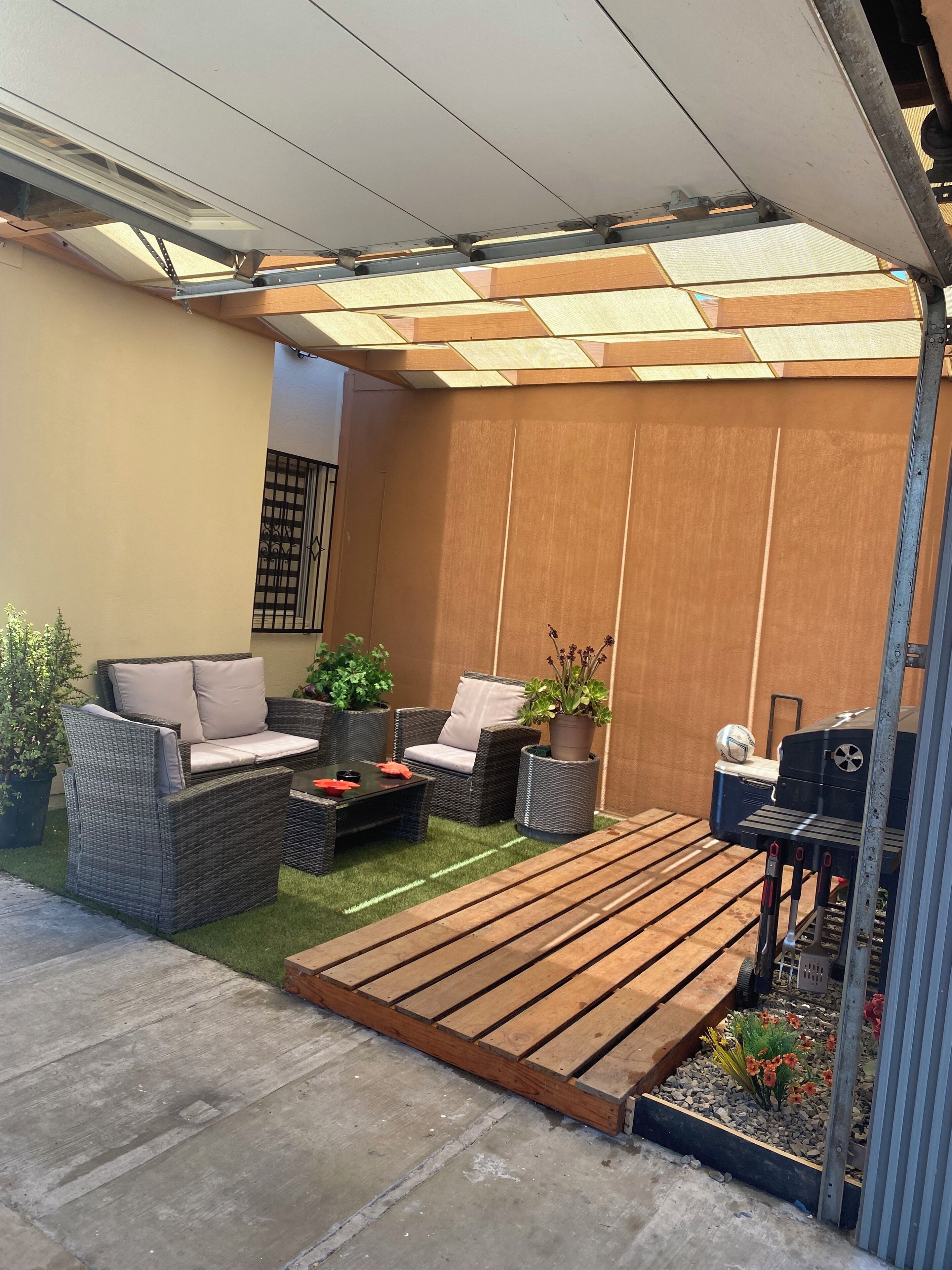 Een terras met rieten meubels, een tafeltje en een barbecue.