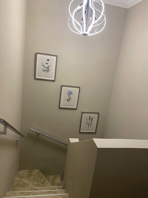 Un escalier avec une main courante, un luminaire et trois illustrations botaniques encadrées accrochées au mur.