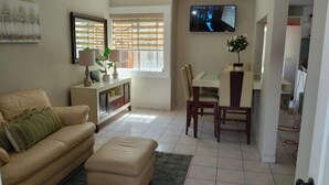 A living room with a sofa, a dining table with chairs, a TV mounted on the wall, and a window with blinds. - Fabulous 3-bedroom house in enjoyable Ensenada for your getaway (Ensenada)