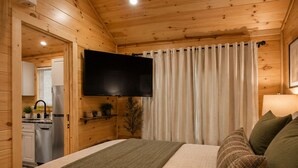 Une chambre confortable, aménagée dans le style d’un chalet, avec un lit en mezzanine, un téléviseur à écran plat et une vue sur la cuisine.