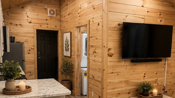 L’intérieur chaleureux d’un chalet, avec un décor en bois, un coin cuisine, un bar et un téléviseur fixé au mur.