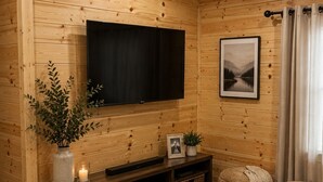 L’intérieur d’un chalet confortable, avec des murs en bois, un téléviseur à écran plat, un tableau encadré, des paniers en osier et un tapis moelleux.