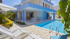 Ein modernes, zweistöckiges Haus mit Swimmingpool, Außenbereich-Sitzgelegenheiten und einer überdachten Terrasse.