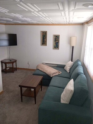 Una sala de estar con un sofá modular, una mesa de centro, un televisor y dos cuadros en la pared.