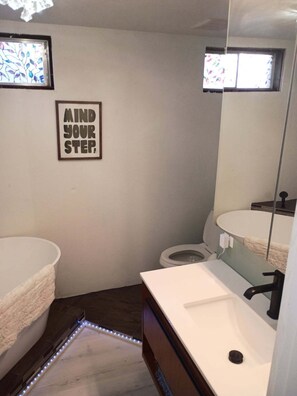 Un baño con lavamanos blanco, inodoro, espejo y una cita inspiradora en el marco en la pared.