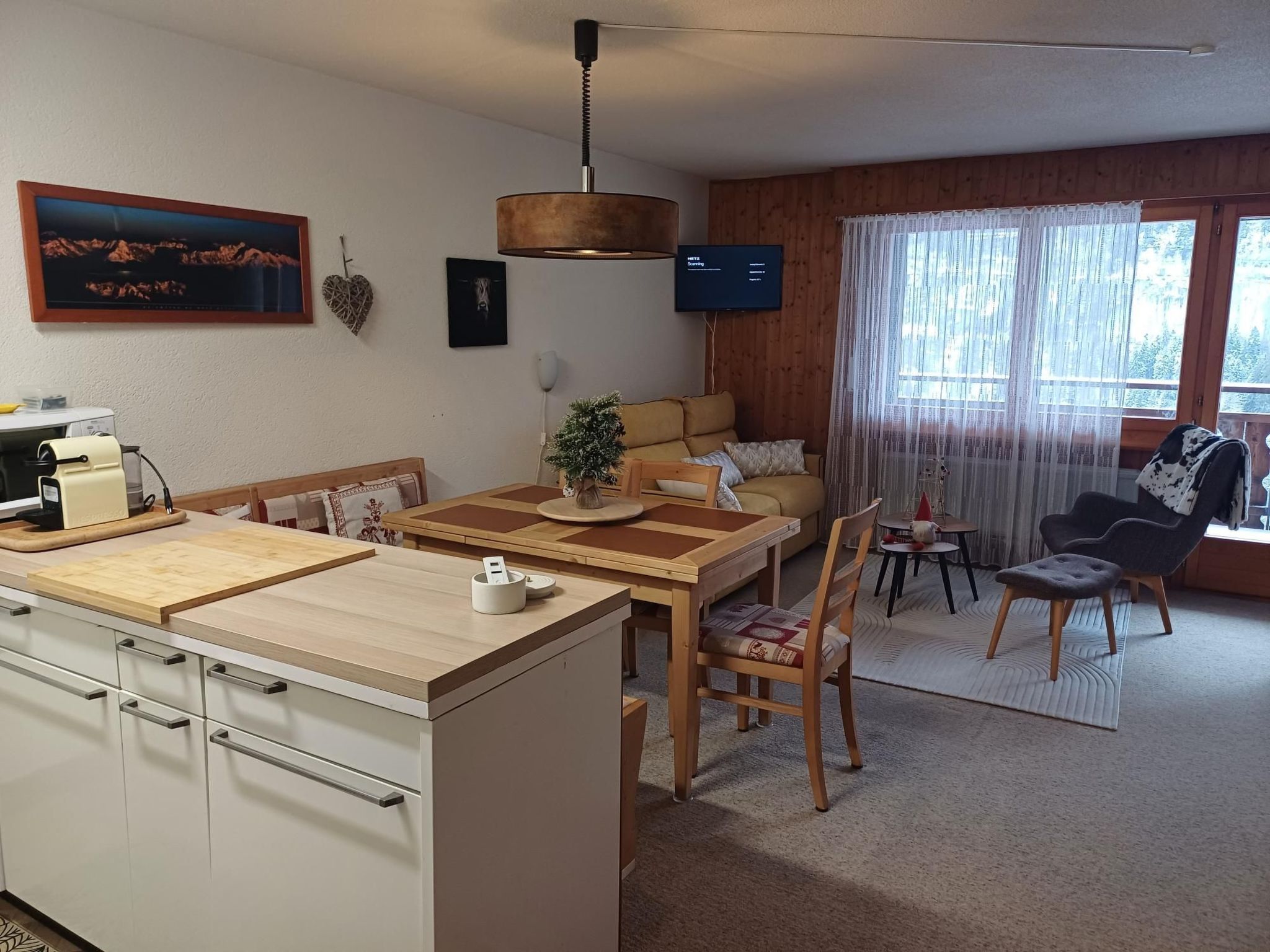 Cozinha moderna com área de jantar, sofá e televisão.