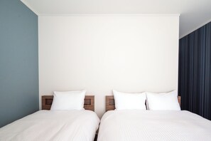 Habitación doble con dos camas, cabeceros de madera y una pared lisa.
