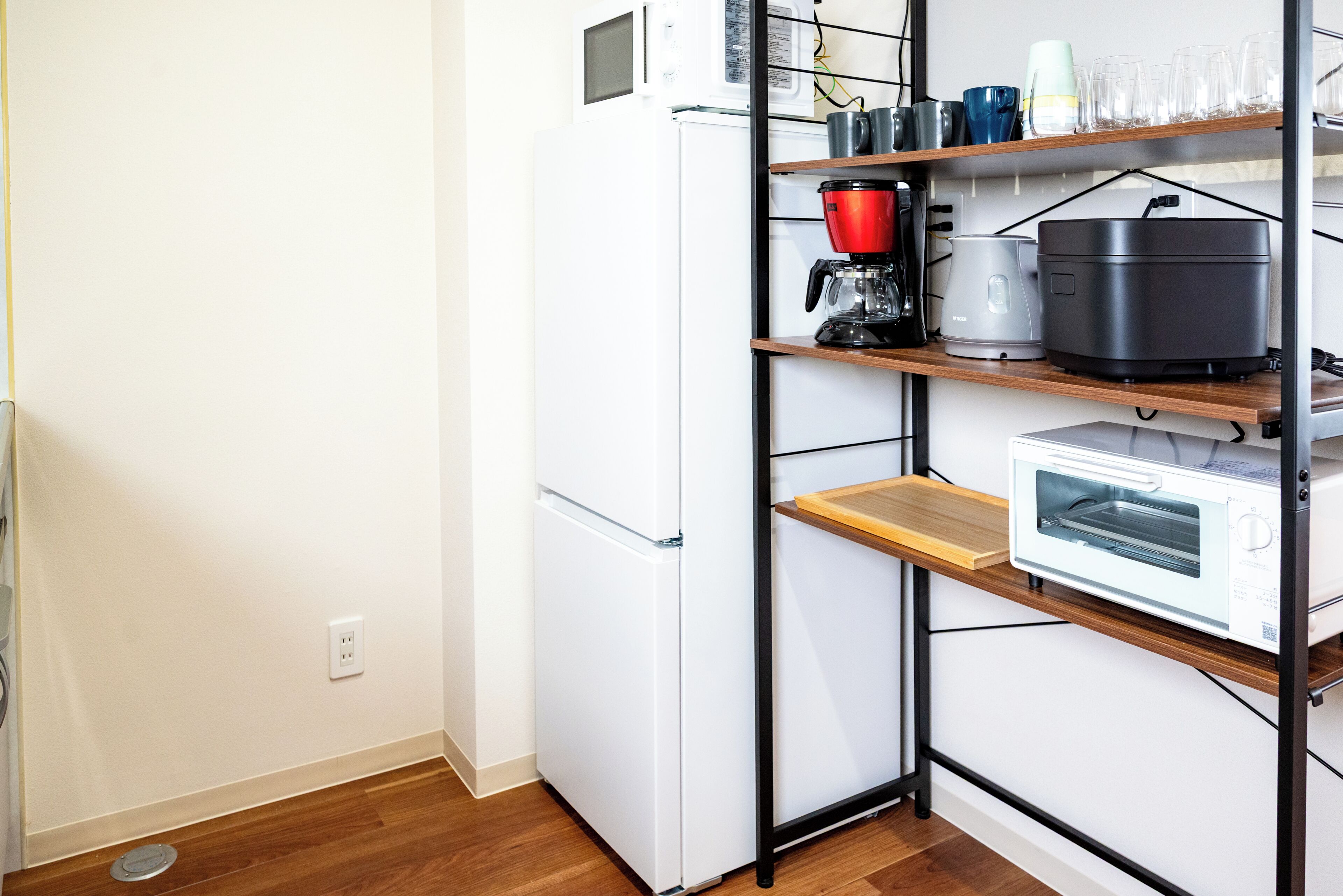 A compact kitchen with a white refrigerator, a coffee maker, a rice cooker, and a microwave on a shelf.
