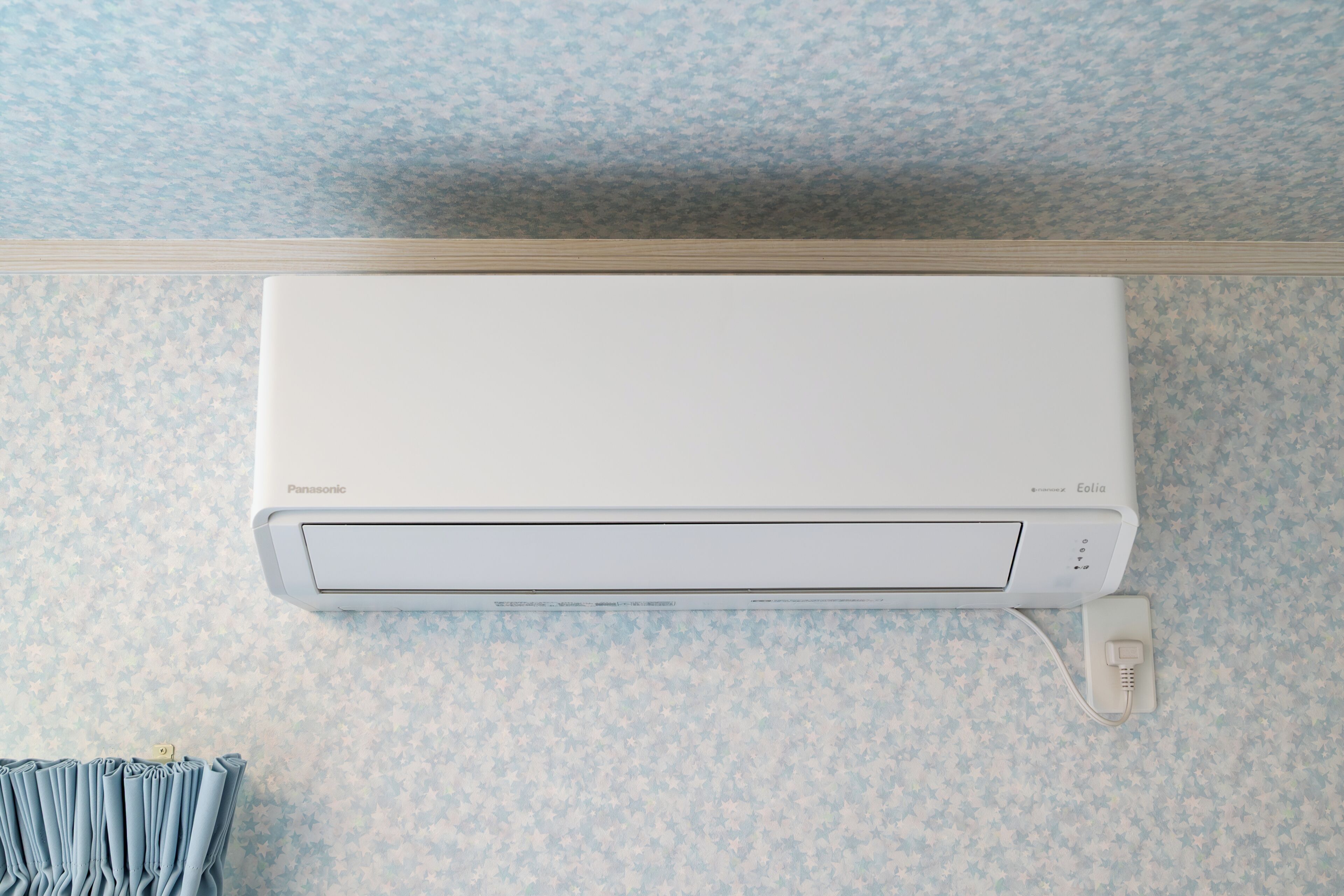 A white air conditioner mounted on a wall with a patterned wallpaper background.