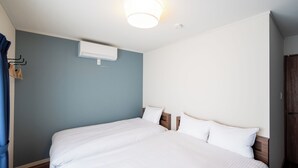 Cama doble con ropa blanca, una lámpara en el techo, un equipo de aire acondicionado y un armario de madera.