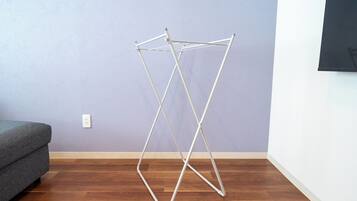 Une pièce avec un plancher en bois, un canapé gris et un étendoir à linge en métal blanc adossé à un mur violet.