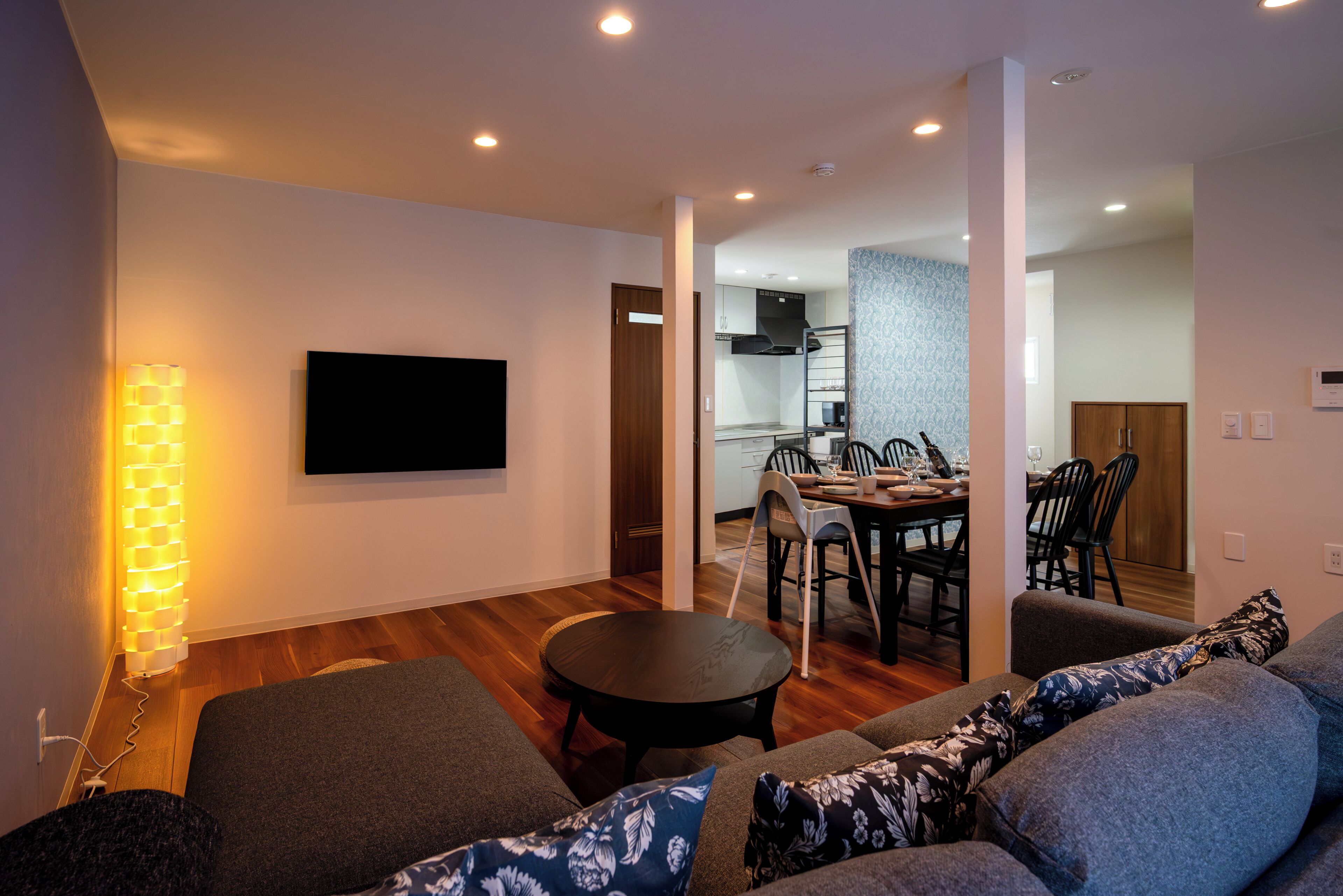 Una sala moderna con un televisor de pantalla plana, un comedor con mesa y sillas, y una cocina al fondo.