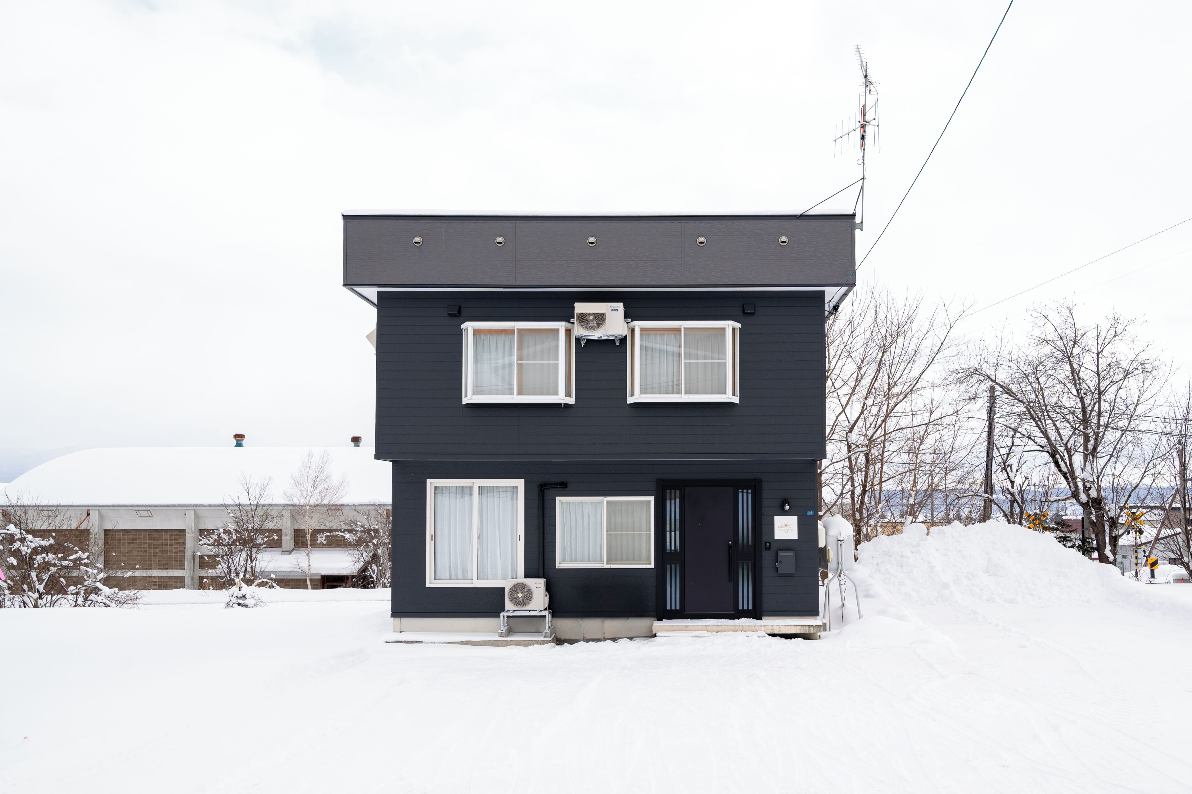 A two-story building with a dark exterior, a black door, and two windows with white frames.