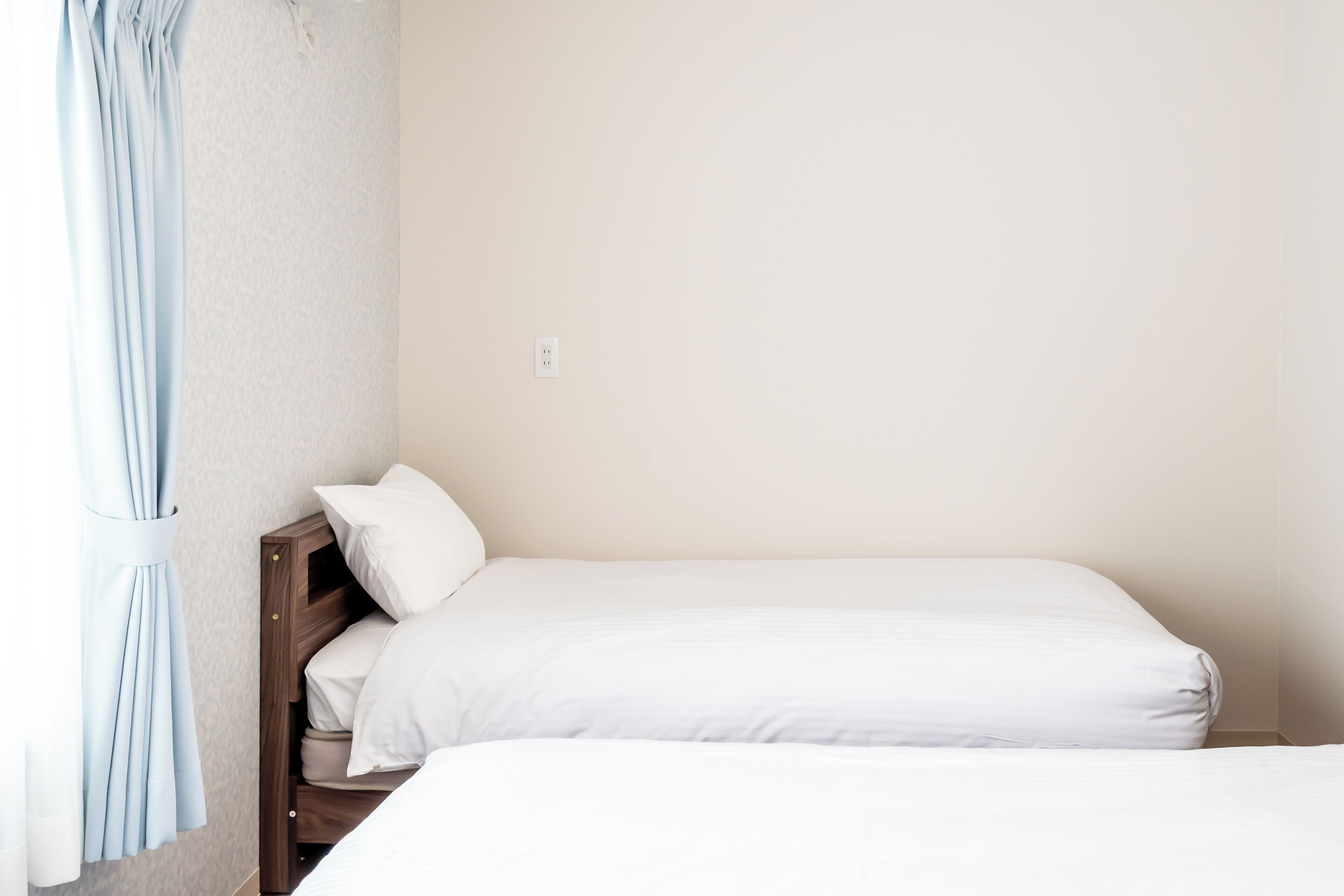 A single bed with white bedding, a wooden headboard, and a light blue curtain.