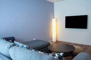 A modern living room with a grey sofa, a round coffee table, a floor lamp, and a flat-screen TV mounted on the wall. - Villa Shigin (Sorachi-gun,Nakafurano-cho)