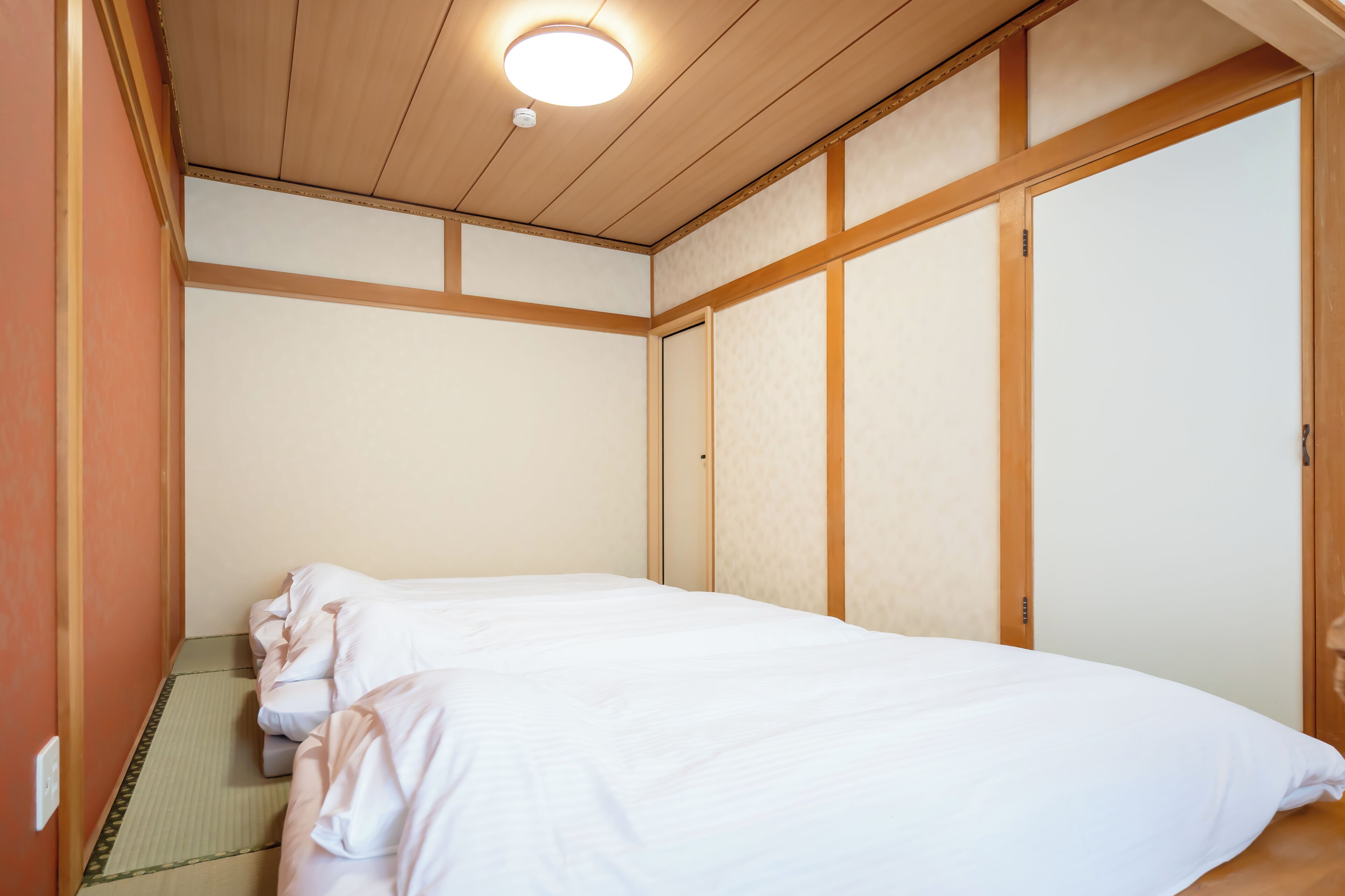 A room with a bed, wooden walls, a ceiling light, and a sliding door.