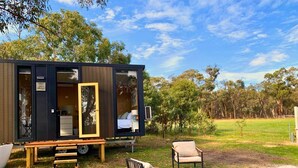 Una casa móvil moderna y compacta con terraza de madera, una mesa de comedor, dos sillas y un pequeño espacio de estar al aire libre.