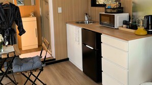 Cocina compacta con microondas, pileta y heladera pequeña. Hay una ventana sobre la pileta y una puerta que da a otra habitación.