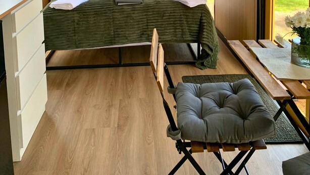 Un dormitorio moderno con cama, lámparas de noche, cabecera de madera, ventana con vistas y una pequeña mesa con una silla.
