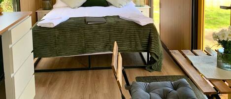 A modern bedroom with a bed, bedside lamps, a wooden headboard, a window with a view, and a small table with a chair.