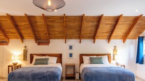 Ein Zimmer mit zwei Holzbetten, Holzbalkendecke, einem kleinen Tisch und einer Wandleuchte.