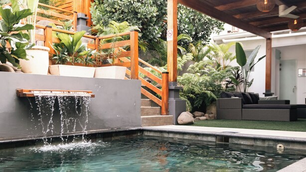 Ein Pool mit Wasserfall, umgeben von Kübelpflanzen und einer Holztreppe.