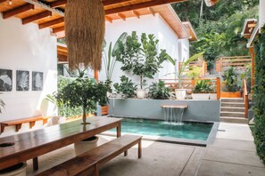 Um pátio moderno ao ar livre com piscina, bancos de madeira e diversos vasos de plantas.
