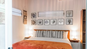 Ein ordentlich bezogenes Bett mit einer gemusterten Decke, eine Wand mit gerahmten Kunstwerken und ein Nachttisch mit einer Lampe.