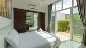 A hotel room with a bed, a ceiling fan, a large window with curtains, and a view of greenery outside. - Private Pool Villa Oxygen Bangtao 3BR (Tambon Choeng Thale)